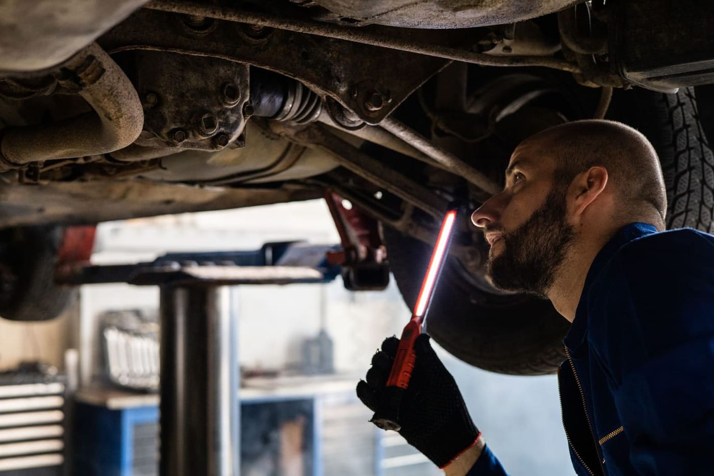 Monteur bekijkt met een looplamp de onderkant van een auto op de brug